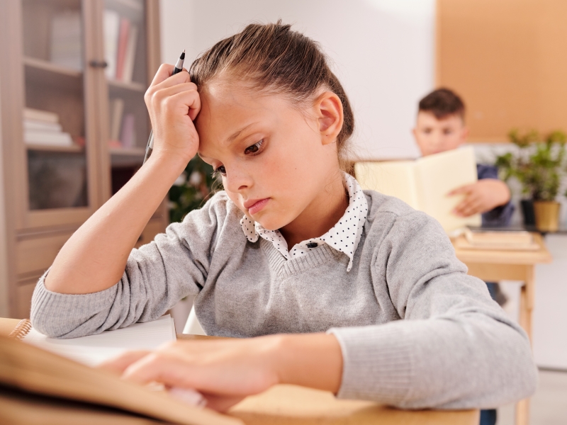 Mädchen sitzt ratlos vor der Klassenarbeit und greift sich an den Kopf