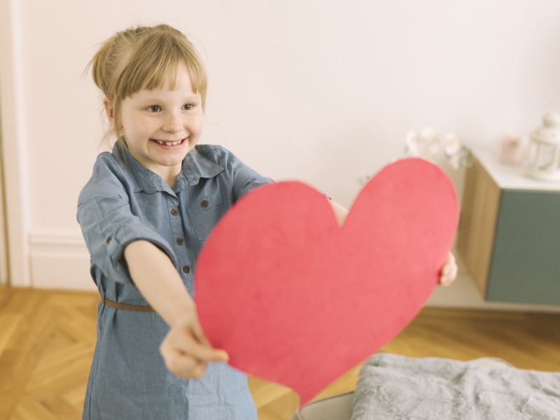 Liebevolle Arbeit mit Kindern Kind hält fröhlich ein rotes Herz in den Händen