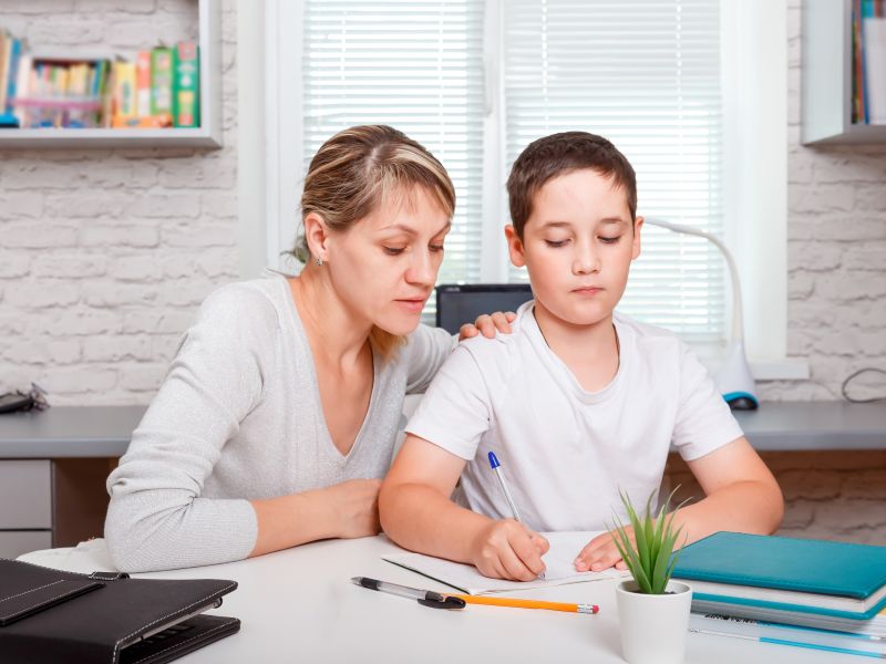 Mutter hilft bei den Hausaufgaben Mutter hilft ihrem Sohn bei den Hausaufgaben am Schreibtisch
