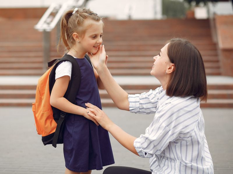 Mutter verabschiedet ihre Tochter aufmunternd vor der Schule